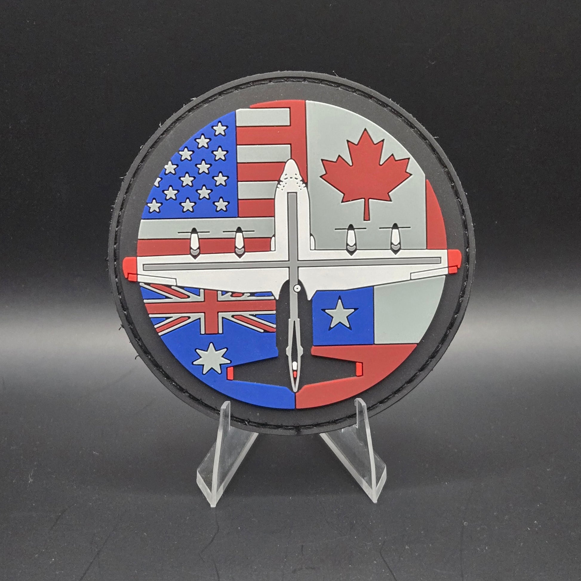 A round embroidered patch featuring an airplane and flags of different countries. Canada USA Australia Chile