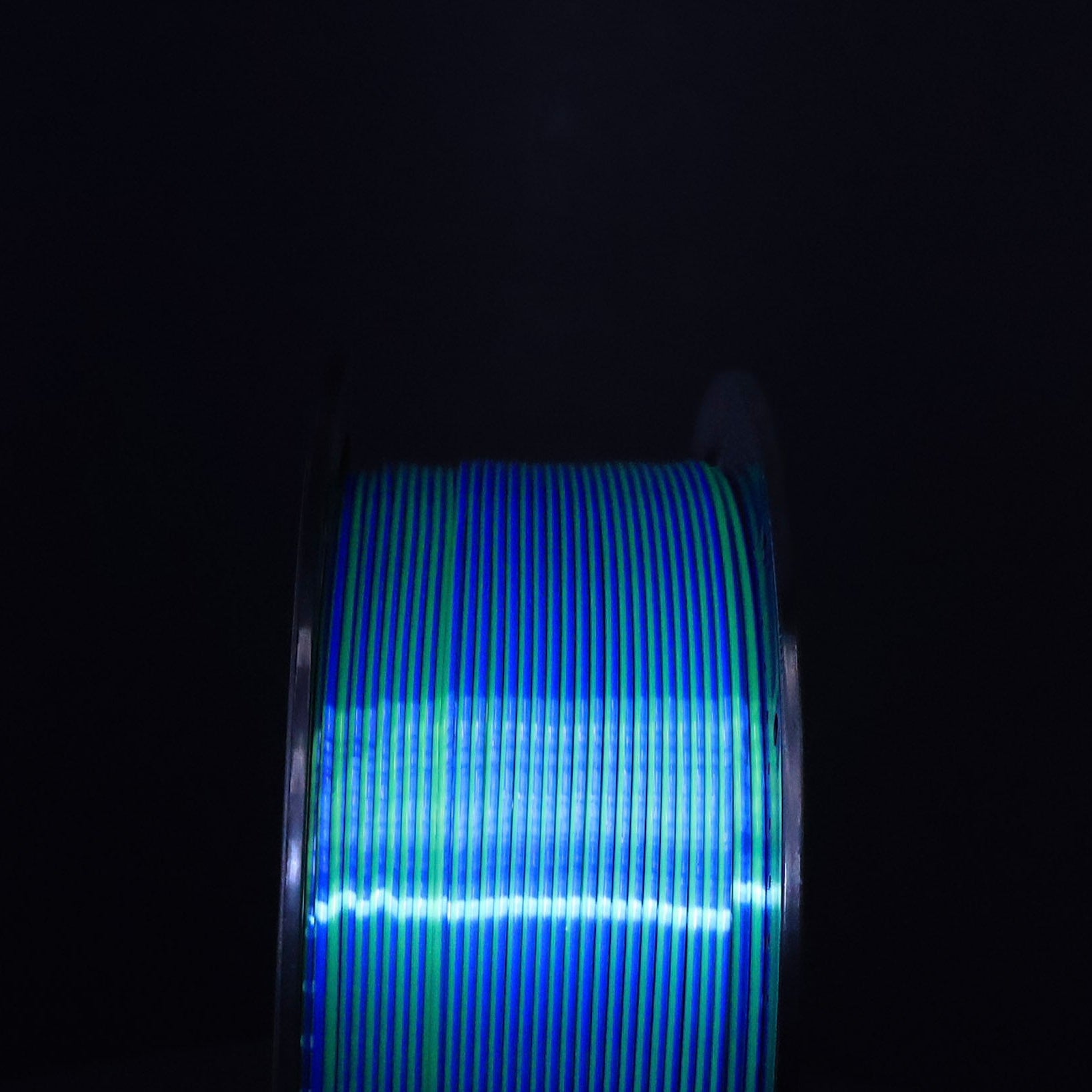 Head on view of a Spool of Silk Blue and Green PLA Filament against a black background. Dual Colored PLA