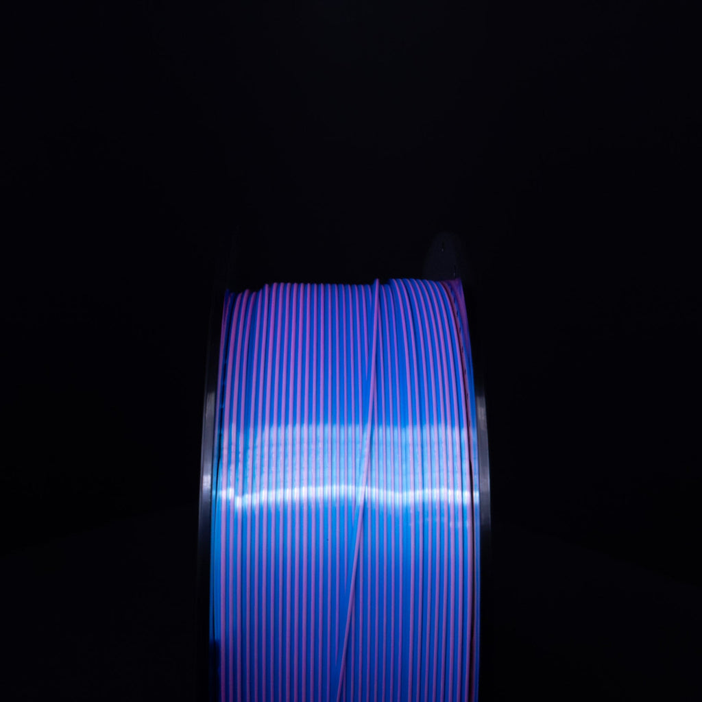 Head on view of a Spool of Silk Blue and Pink PLA Filament against a black background. Dual Colored PLA