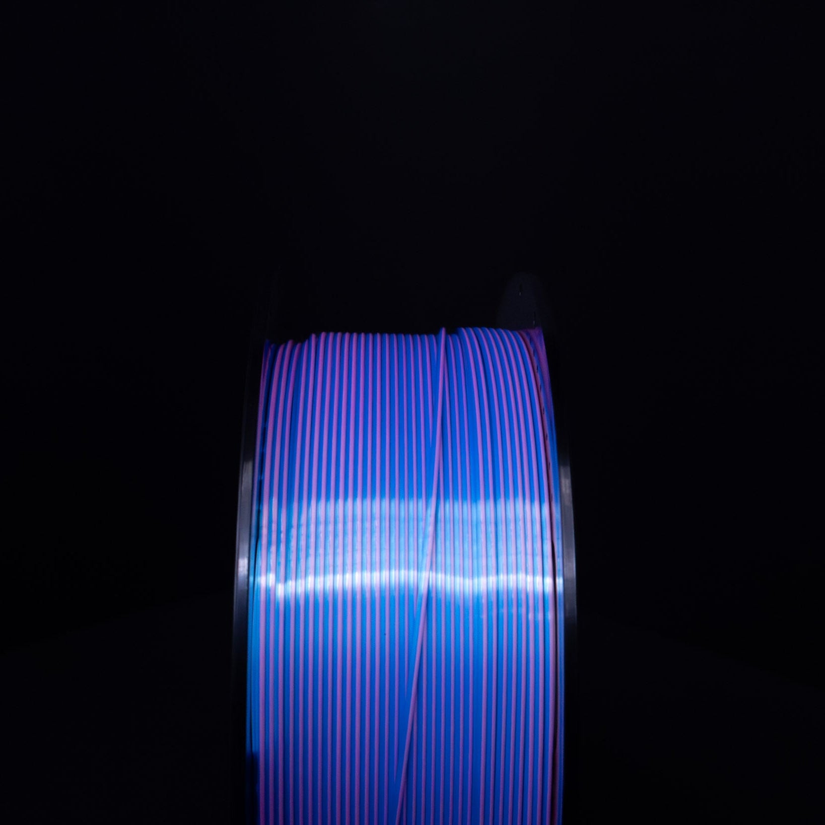 Head on view of a Spool of Silk Blue and Pink PLA Filament against a black background. Dual Colored PLA