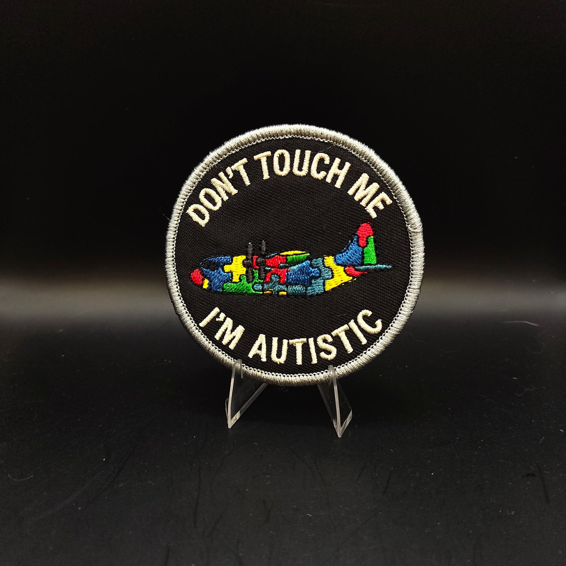 Patch with 'Don't Touch Me I'm Autistic' text and colorful symbols on a black background