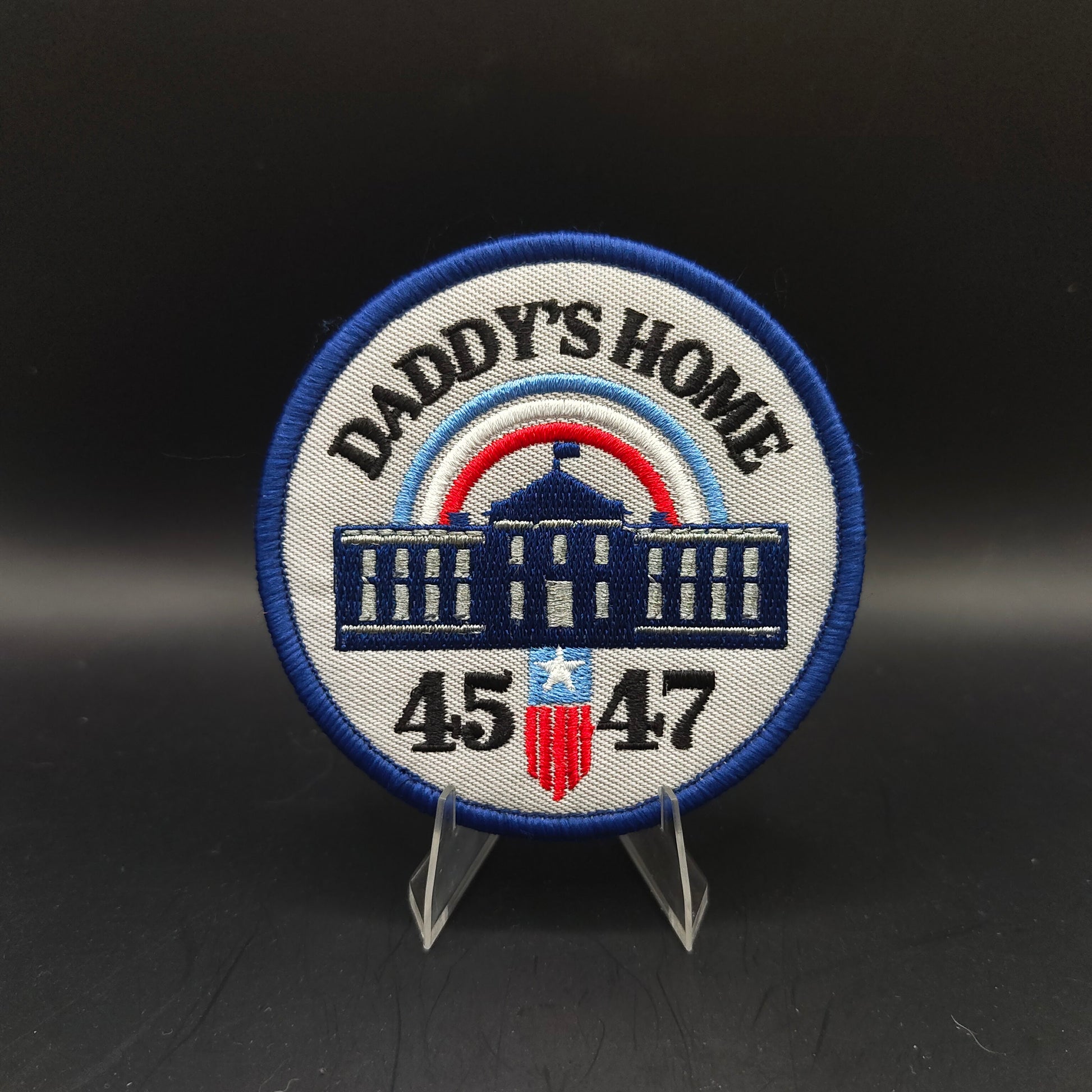 Patch with 'Daddy's Home' text and numbers on a stand against a dark background Trump Patch 45 47