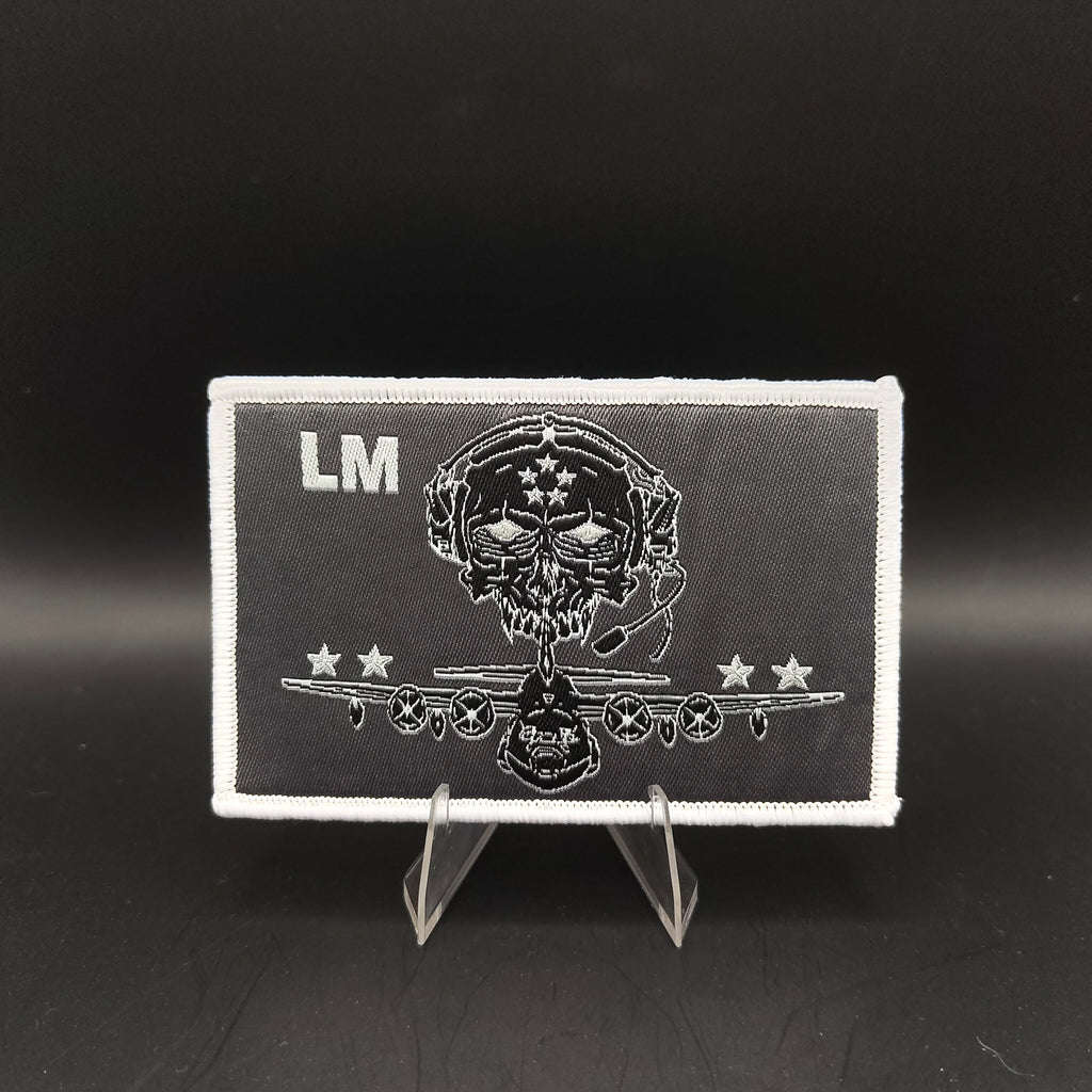 Black and white patch with skull design and 'LM' initials on a stand against a black background loadmaster aircrew kc-130j c-130 crew patch